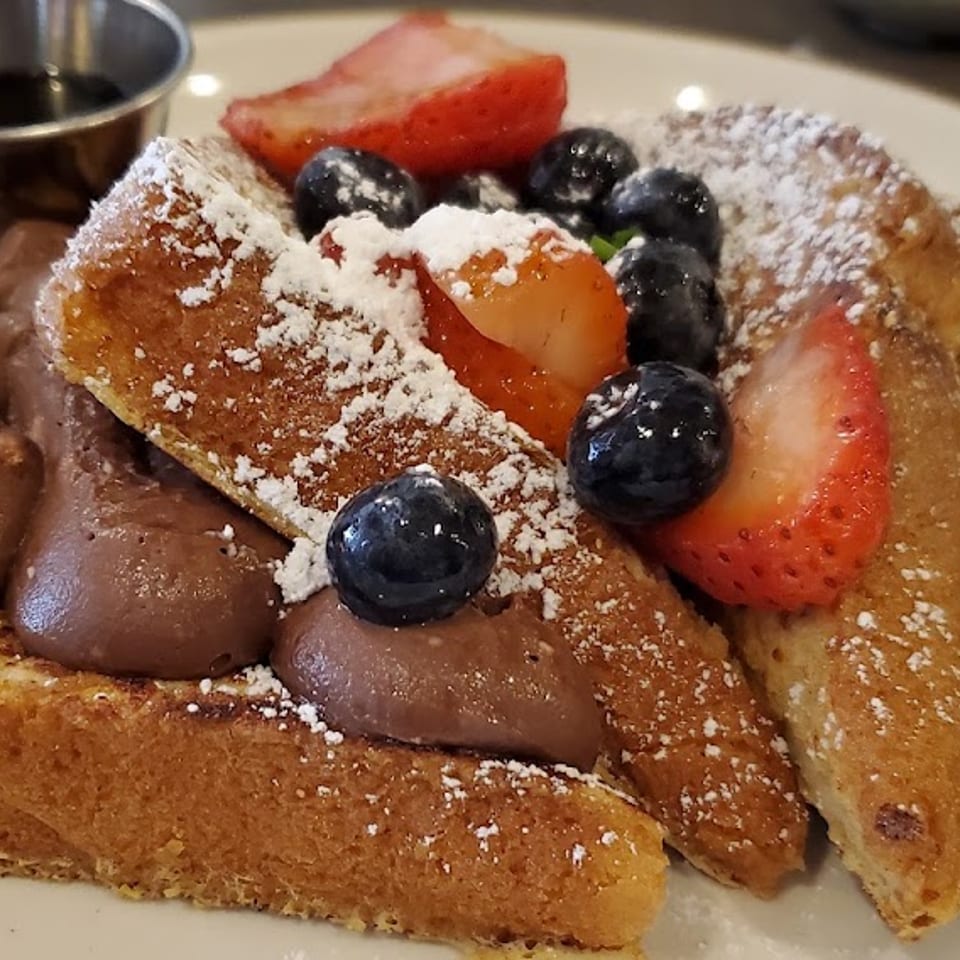 French toast topped with chocolate cream, powdered sugar, strawberries, and blueberries, with syrup.