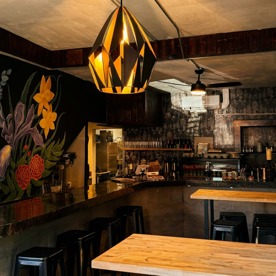 A restaurant interior with a floral mural, a bar, and wooden tables with black stools.